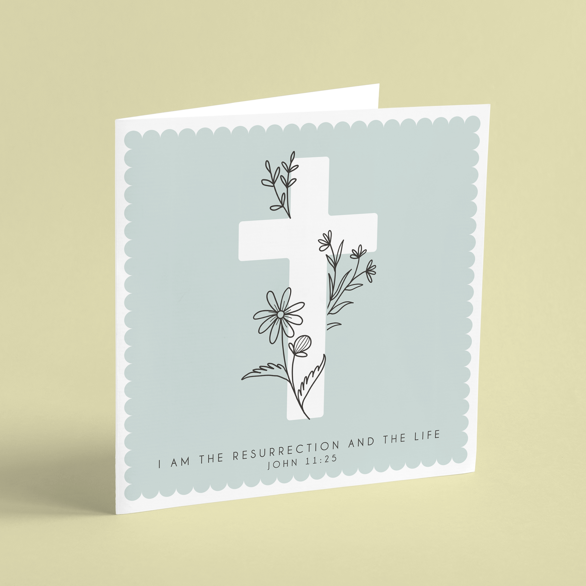 A square Easter card featuring a white cross on a green background illustrated with floral outlines and reading 'I am the resurrection and the life. John 11:25'.